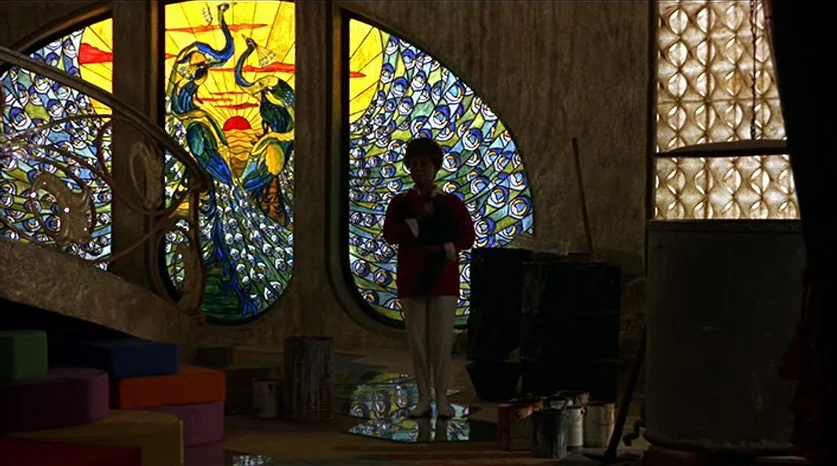 Juliet of the Spirits (1965) movie still: wide — A spacious room features large, ornate stained glass windows depicting peacocks against a sunrise.…