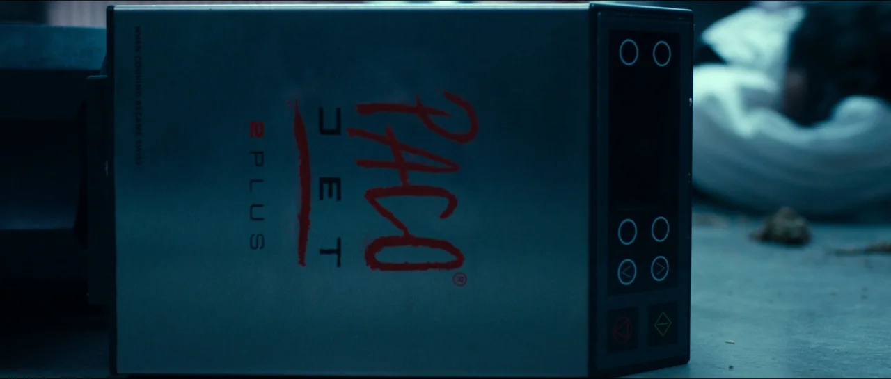 The Menu (2022) movie still: closeup — A metal Pacojet 2 Plus machine rests on its side on a tiled floor. Blurred white shapes are visible in the…