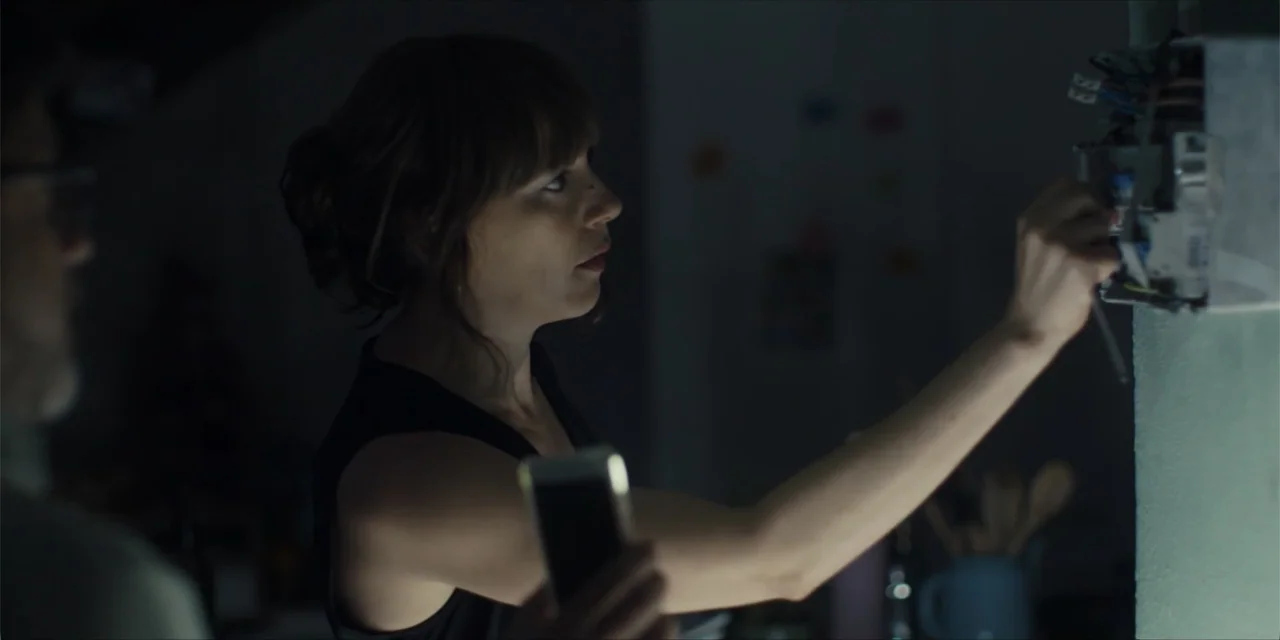 Instant Love (2020) movie still: medium — A dimly lit utility space contains exposed wiring and an open electrical breaker box. A woman in a black…