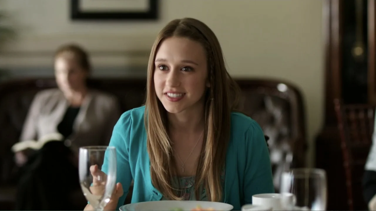 At Middleton (2013) movie still: medium — A well-lit interior dining area with a person seated in the foreground. A young woman smiles while…