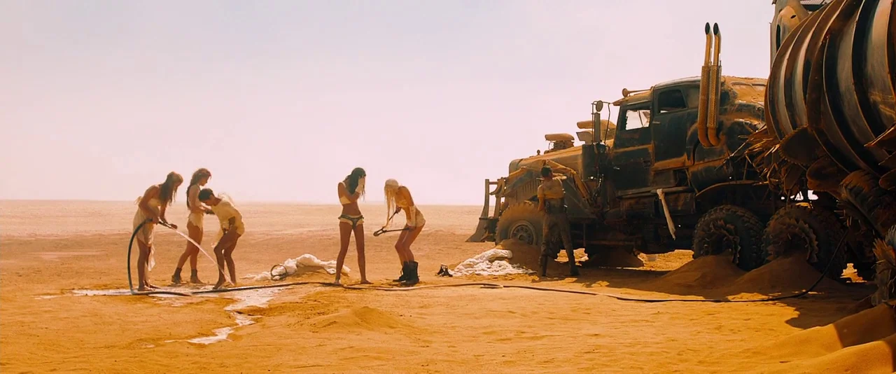 Mad Max: Fury Road (2015) movie still: wide — A flat, expansive desert landscape features a massive, rusted, industrial-style tanker truck. Five…