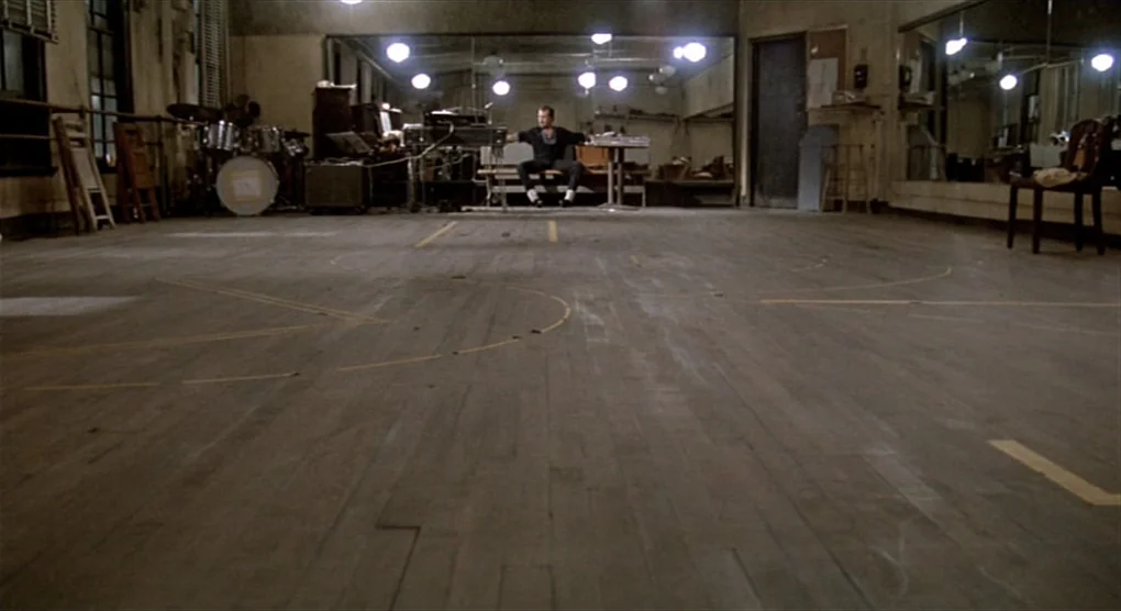 All That Jazz (1979) movie still: wide — A spacious dance studio features a hardwood floor with painted markings and large mirrors. A lone man sits…
