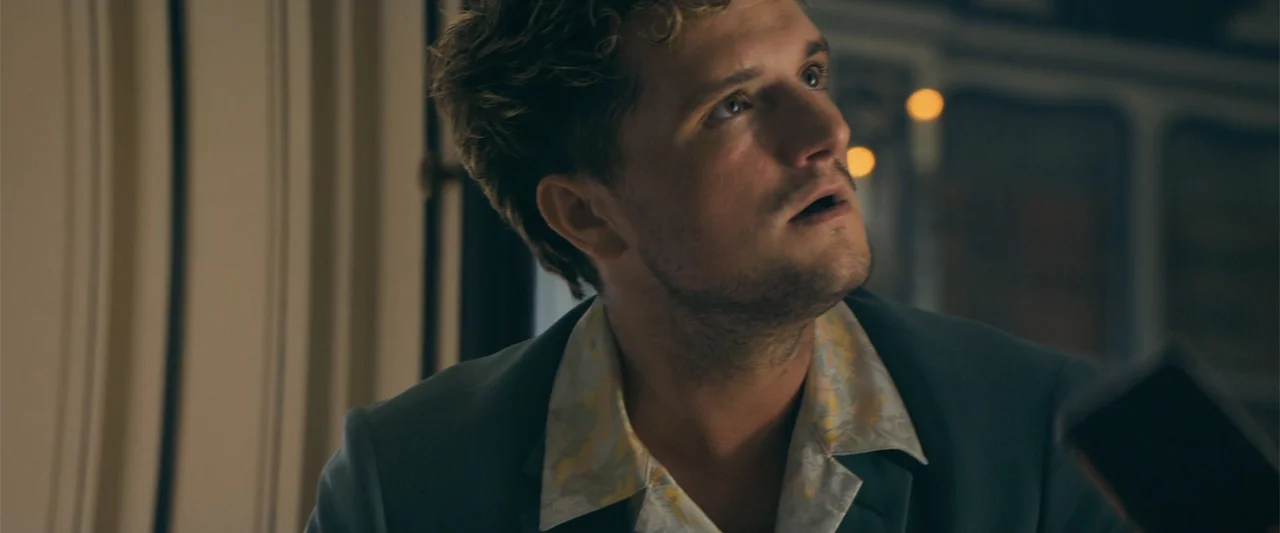 The Beekeeper (2024) movie still: closeup — An interior space with muted tones and a soft, low-key lighting environment. A young man wearing a suit…