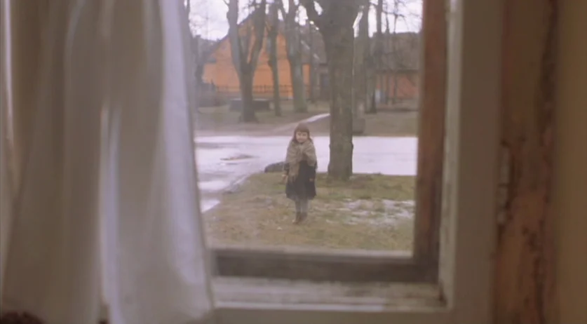 Invincible (2001) movie still: wide — A small girl stands alone on a grassy patch outside a weathered window. The view is framed by a white curtain…