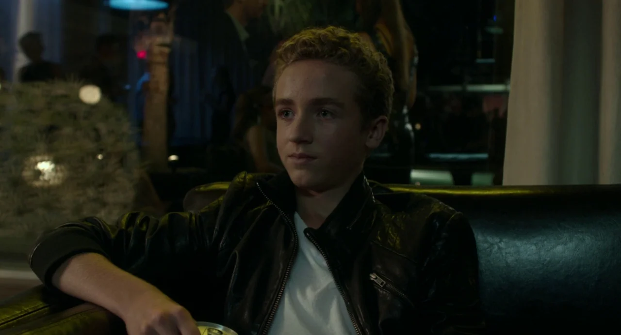 Maps to the Stars (2014) movie still: medium — A dimly lit club setting features blurred silhouettes of people in the dark background. A young male…
