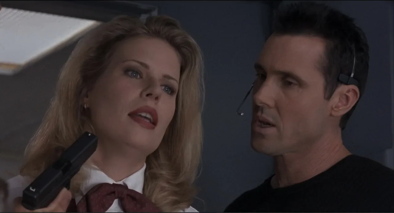 Air Rage (2001) movie still: medium — An interior space features two individuals engaged in a direct confrontation. A blonde woman points a pistol…