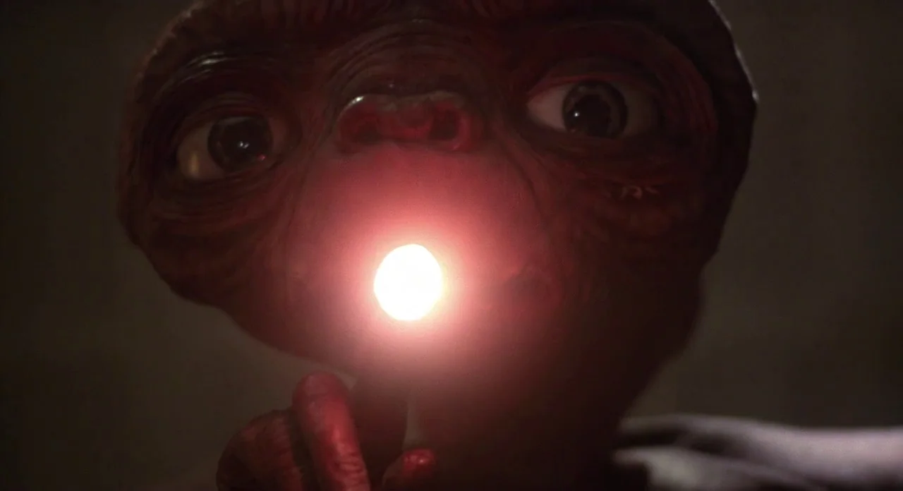 E.T. The Extra-Terrestrial (1982) movie still: closeup — An alien creature with wrinkled skin and large eyes dominates the dark, unidentifiable…