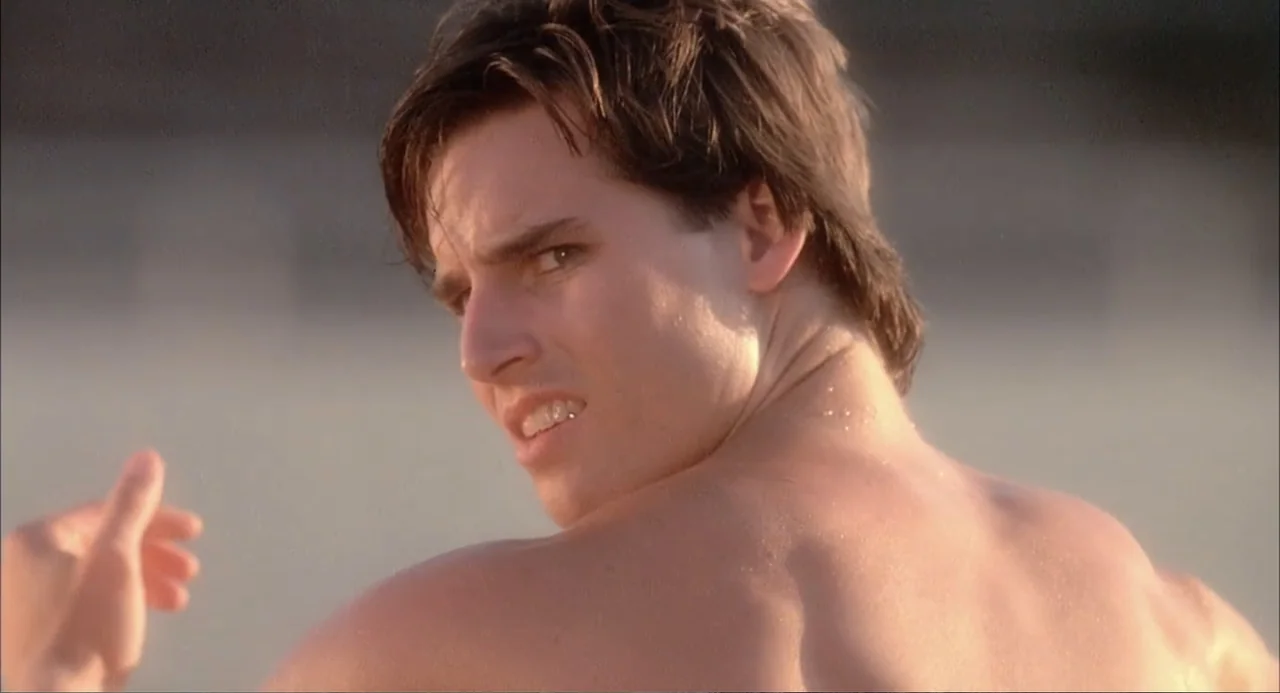 Teen Witch (1989) movie still: closeup — A sunny, bright exterior beach setting with a soft, out-of-focus background. A young man with dark hair…