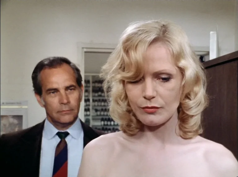 Fear Of Fear (1975) movie still: medium — An interior office space with a blurred storage area visible in the background. A woman with blonde hair…