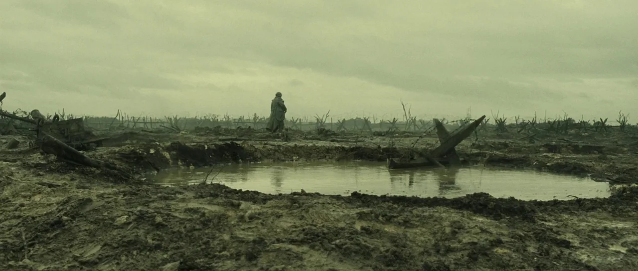 A Very Long Engagement (2004) movie still: wide — A desolate, mud-filled landscape under a heavy overcast sky features scattered debris. A lone…