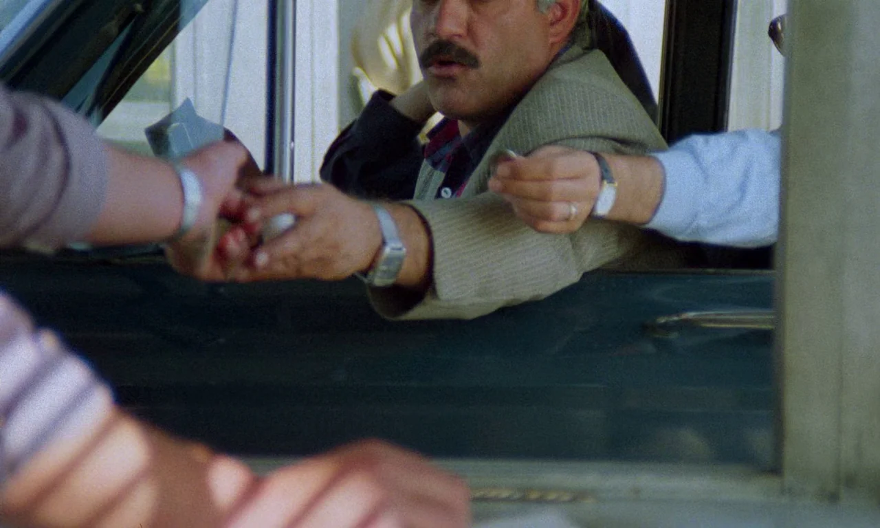Life, and Nothing More (1992) movie still: medium — A man sits inside a vehicle at a toll booth window with metal frames. He reaches out his hand to…