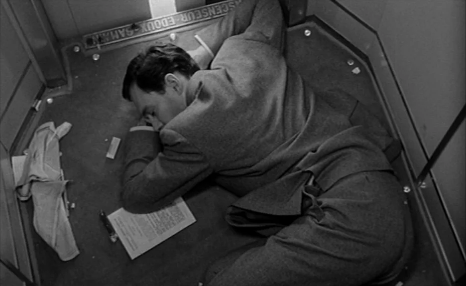 Elevator To The Gallows (Ascenseur pour l’échafaud) (1958) movie still: fullbody — A small square elevator cabin features metal surfaces and a paper…