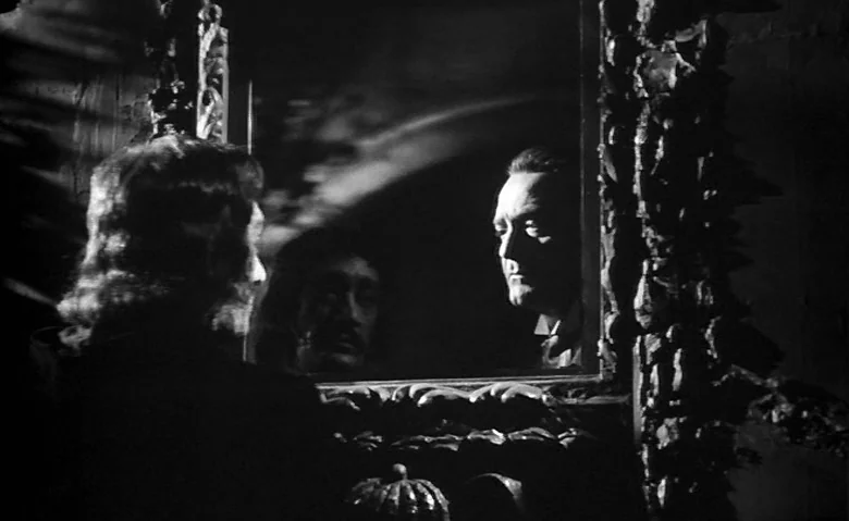 Black Sunday (1960) movie still: medium — A dark, dimly lit room contains an ornate, textured wooden frame mirror. A man gazes into the reflective…