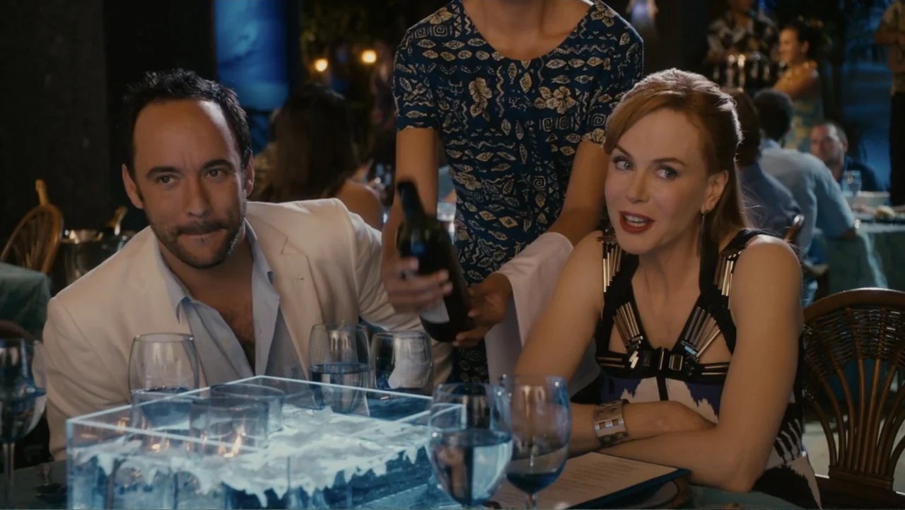 Just Go with It (2011) movie still: medium — A well-lit tropical restaurant features a dining table in the foreground. A waiter serves wine to a man…