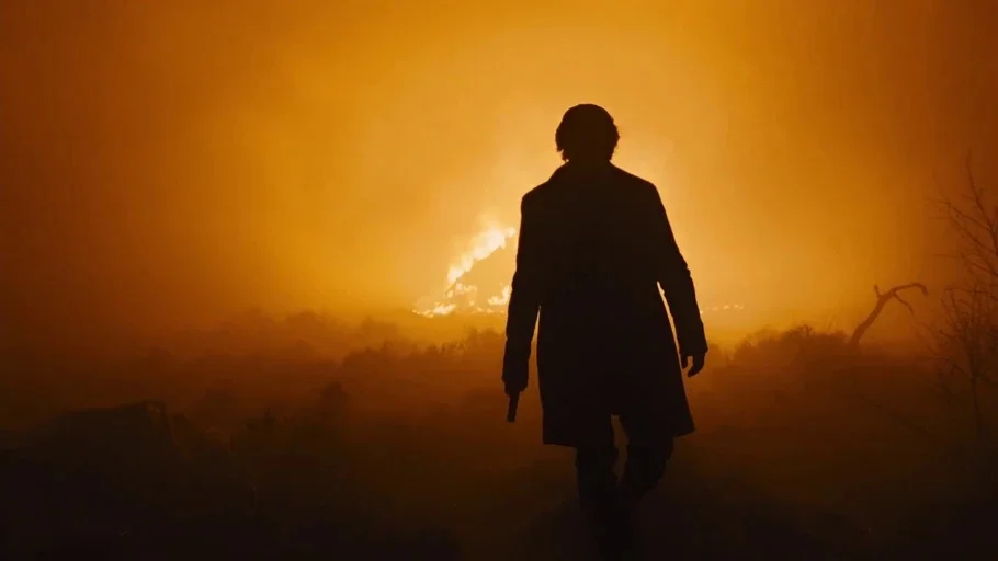 Skyfall (2012) movie still: fullbody — A man stands in a dark, rural field illuminated by a bright distant fire. He walks towards the flames while…