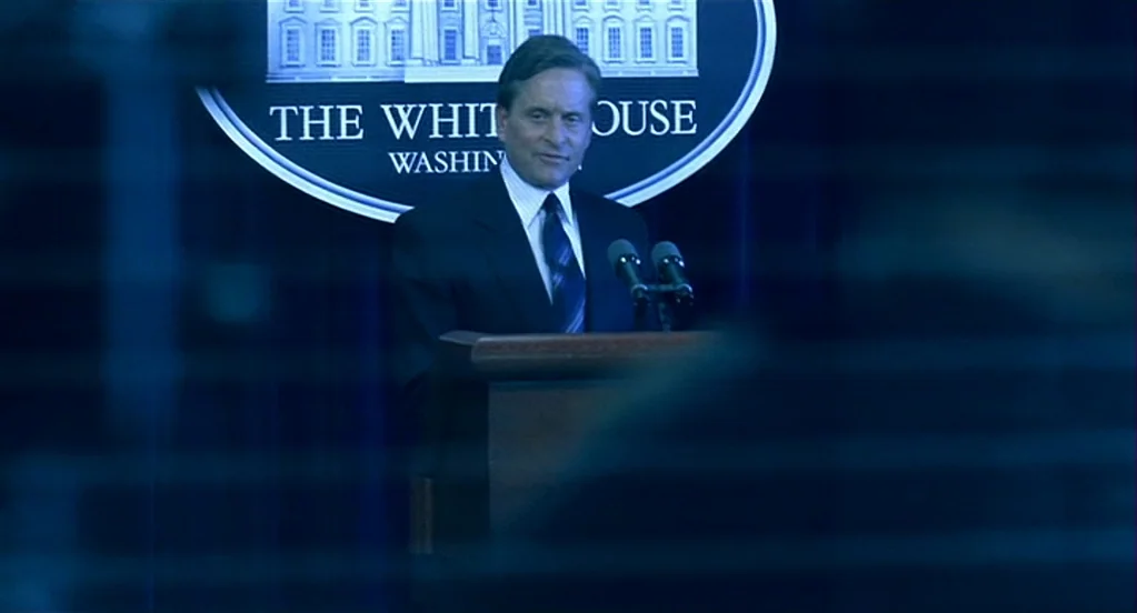 Traffic (2000) movie still: medium — A man stands behind a podium in a dark, navy-blue room. A large White House seal is visible on the wall behind…