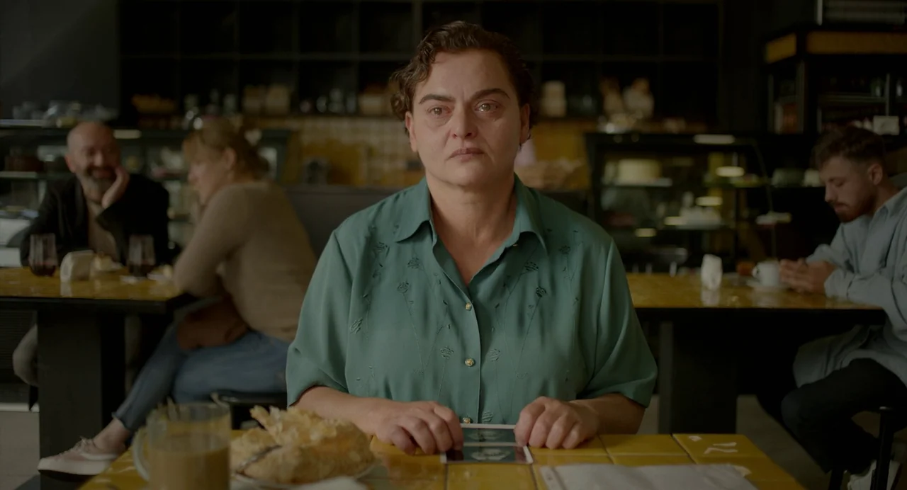 Blackbird Blackbird Blackberry (2023) movie still: medium — A cafe with yellow tiled tables and dark background shelves holds several seated…