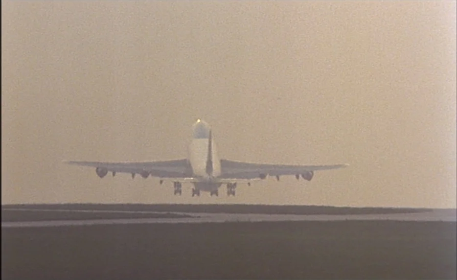 I Want To Go Home (1989) movie still: wide — An airplane takes off from a flat, dark-paved runway into a thick, hazy atmosphere. The horizon is…