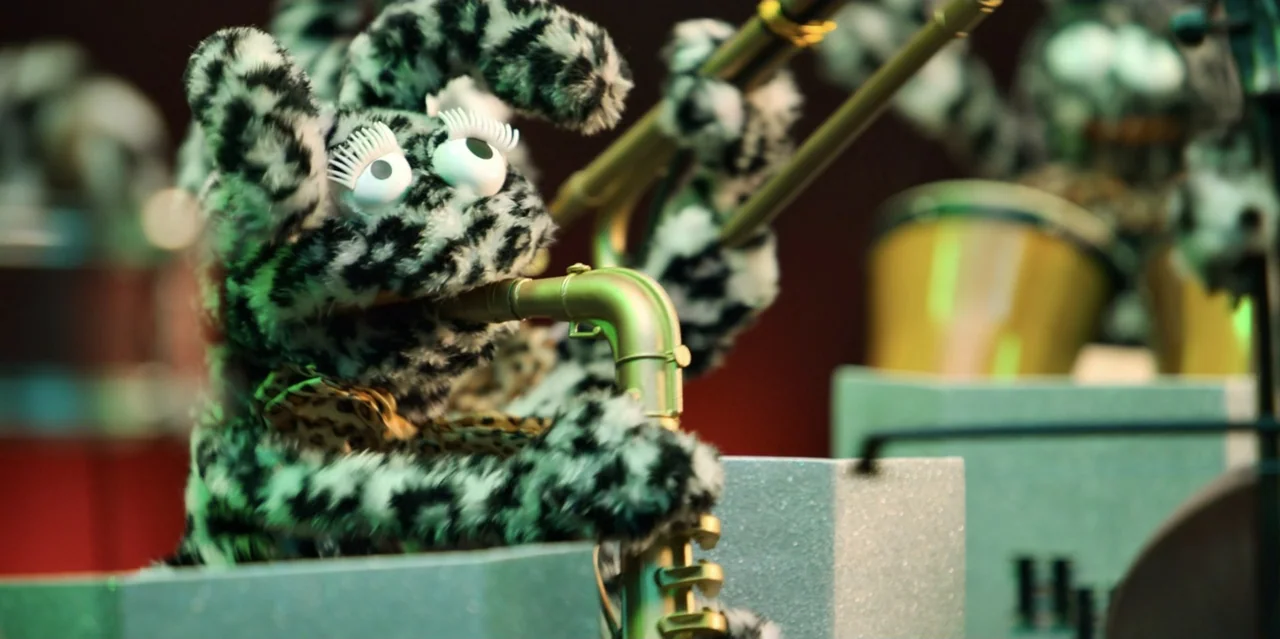 31 Minutes: One Hot Christmas (2025) movie still: closeup — A furry puppet musician performs on a stage with a glittery silver podium. The character…