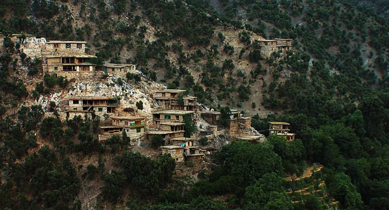 Zero Dark Thirty (2012) movie still: establishing — A cluster of stone houses clings to a steep, forested mountain hillside. The architecture…
