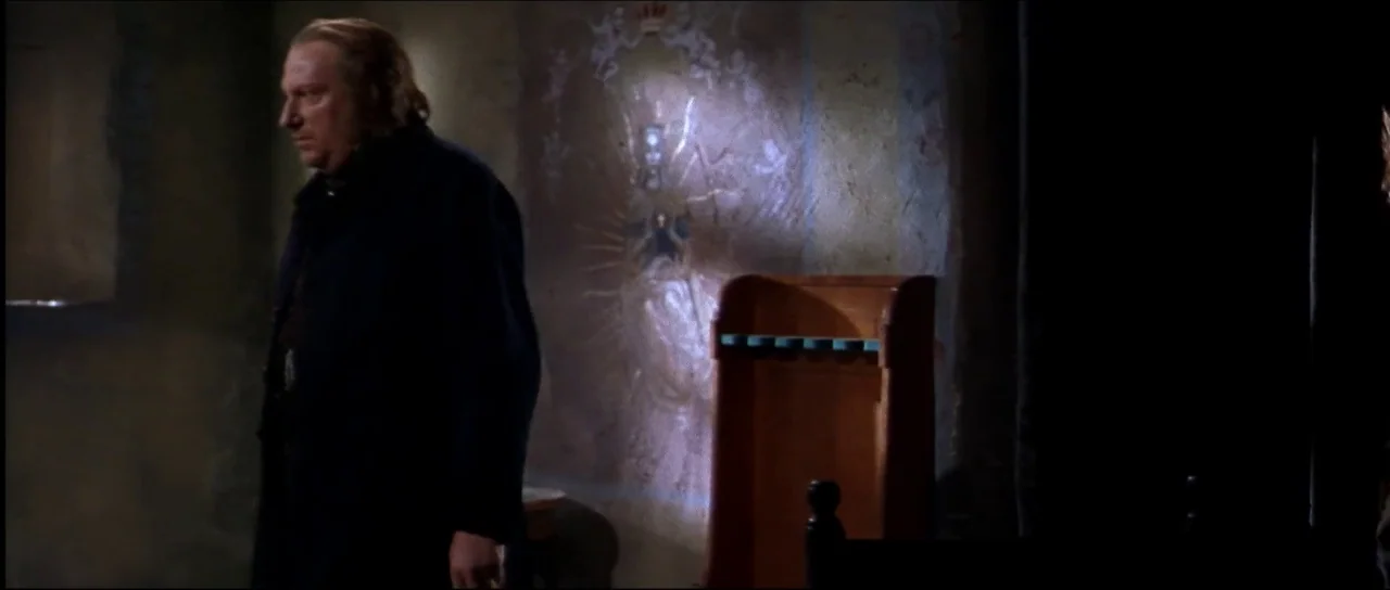Ravenous (1999) movie still: medium — A dimly lit stone chamber features a faded painted religious mural on the wall. A middle-aged man stands in…
