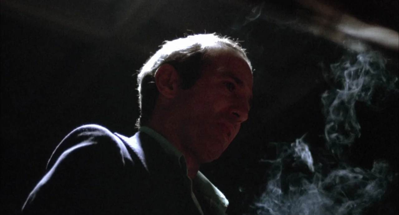 The Killing of a Chinese Bookie (1976) movie still: closeup — A dark indoor setting features a man standing in a patch of concentrated light. The…