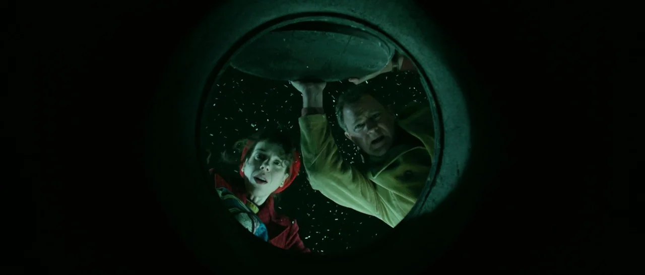 Paddington (2014) movie still: medium — A dark night scene framed from within a manhole looking upward at the street. Two people in colorful coats…