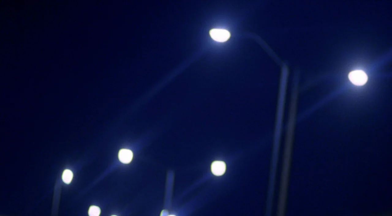 Boys Don’t Cry (1999) movie still: establishing — An array of streetlights illuminates the dark night sky. The lights create a series of blurred…