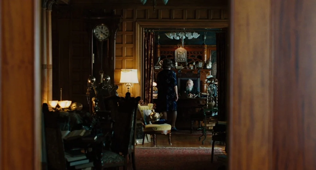 A Serious Man (2009) movie still: wide — A wood-paneled room is filled with classic furniture and antique decorative objects. A woman faces an older…
