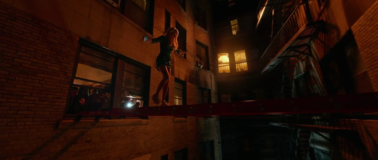 Nerve (2016) movie still: wide — A narrow alleyway between two brick buildings at night features a prominent fire escape. A woman in a sequined…