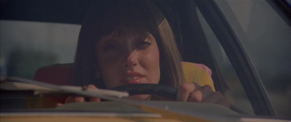 3 Women (1977) movie still: closeup — The interior of a moving vehicle during daylight hours with a blurred exterior. A young woman with brown hair…