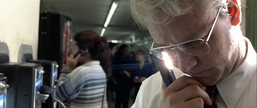 The Insider (1999) movie still: closeup — A long indoor hallway with payphones mounted on the side wall. An older man speaks on a phone while a…