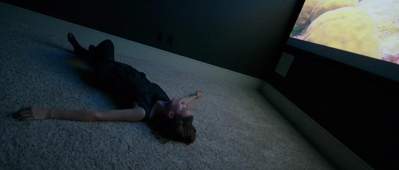 Song to Song (2017) movie still: wide — A dark home theater with wall-to-wall beige carpeting and dark charcoal grey walls. A woman lies flat on her…