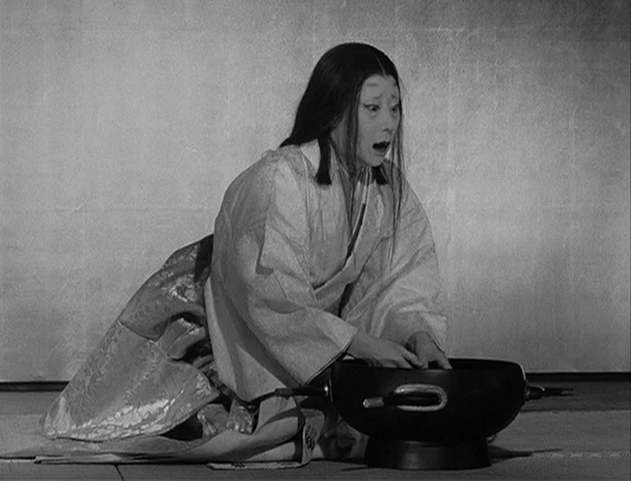 Throne of Blood (1957) movie still: medium — A room with a plain, neutral-toned wall and mat floor. A woman in a traditional patterned kimono kneels…