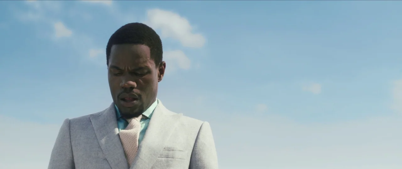 Da Sweet Blood of Jesus (2014) movie still: medium — A man stands outdoors against a clear blue sky with light clouds. He is looking down while…