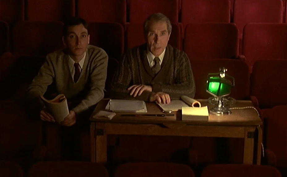 The Last Metro (1980) movie still: medium — A dimly lit room features rows of red velvet seats behind a wooden desk. Two men sit behind the desk…