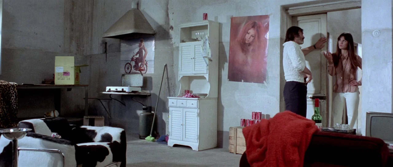 The Suspicious Death of a Minor (1975) movie still: wide — A sparsely furnished room with textured plaster walls and a retro kitchen hutch. A man…
