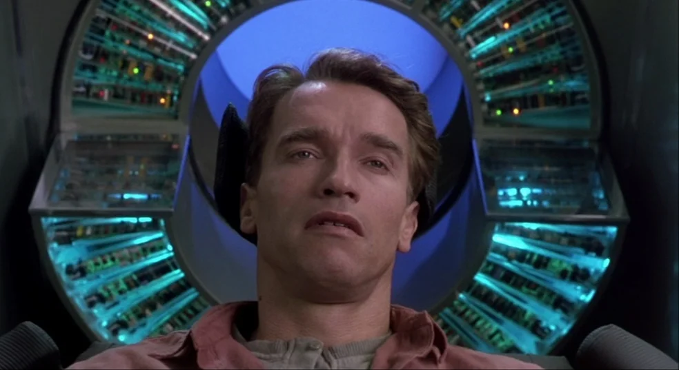 Total Recall (1990) movie still: closeup — A futuristic circular electronic device with glowing blue lights frames a man's head. The man sits…