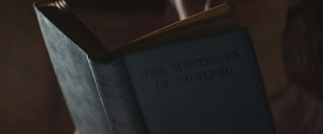 The Wind (2005) movie still: closeup — An open antique book titled The Mysteries of Udolpho lies in a dimly lit room. The pages are fanned out…