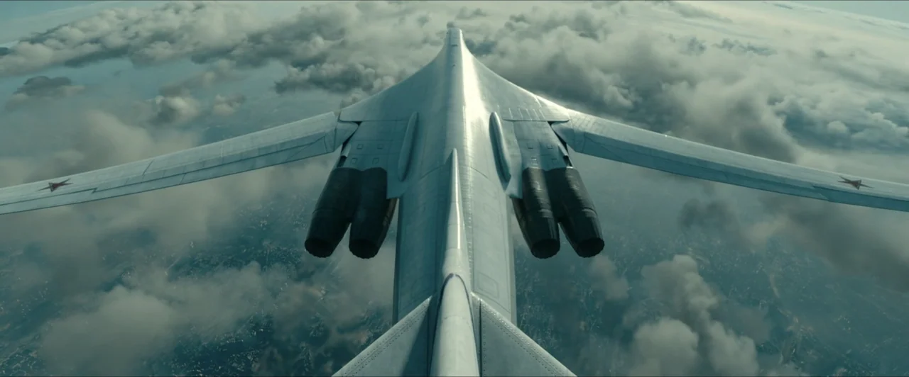 Invasion (2020) movie still: wide — A sleek military aircraft flies above a cloud deck with the ground visible below. The jet is positioned…