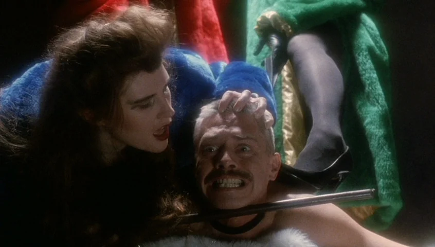 Edward II (1991) movie still: medium — A dark environment with vibrant colored clothing in blue, green, and red textures. A woman leans over a man…