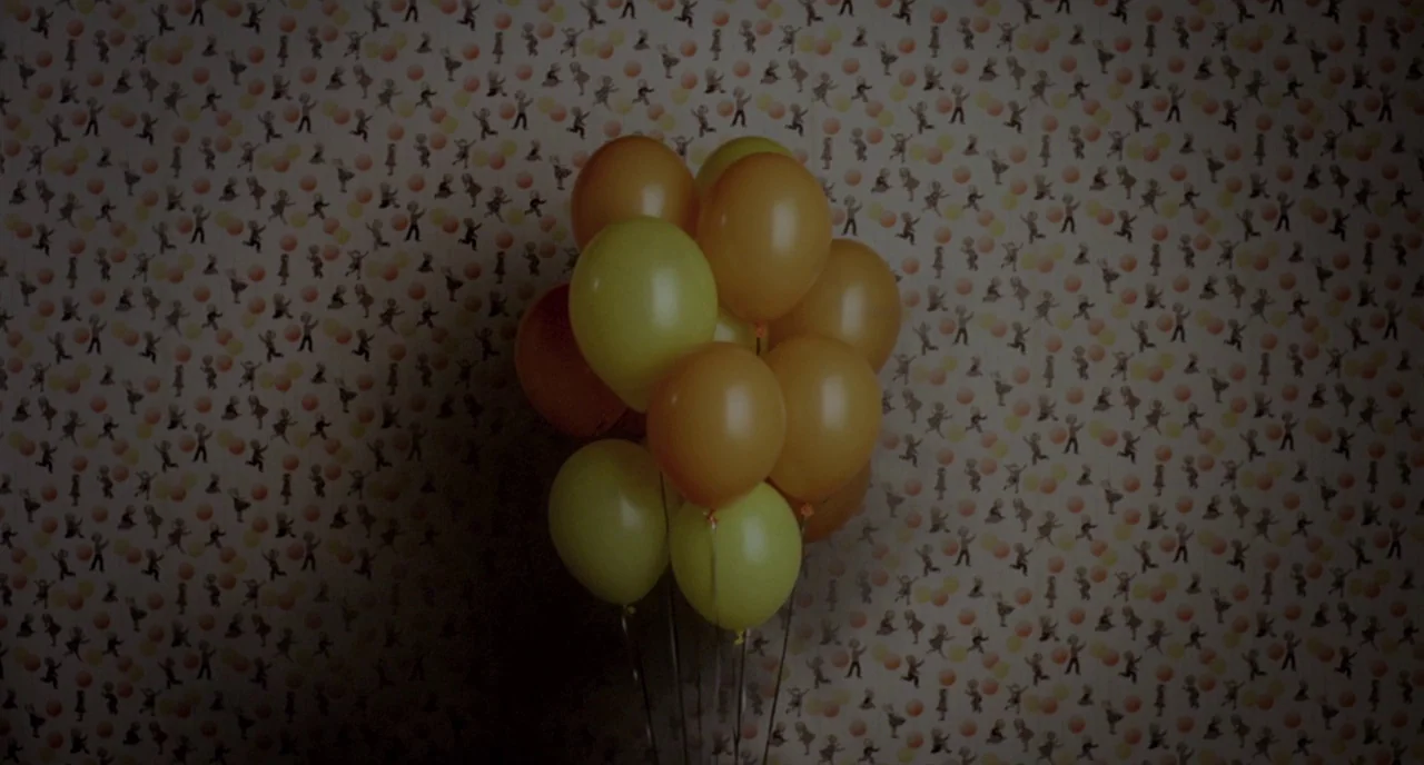Possum (2018) movie still: medium — A cluster of yellow and orange balloons hangs in front of patterned nursery wallpaper. The background is covered…