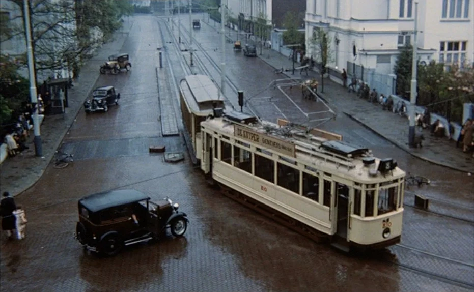 Soldier of Orange (1977) movie still: wide — A rain-slicked city intersection features a cream-colored vintage tram and several 1930s automobiles.…