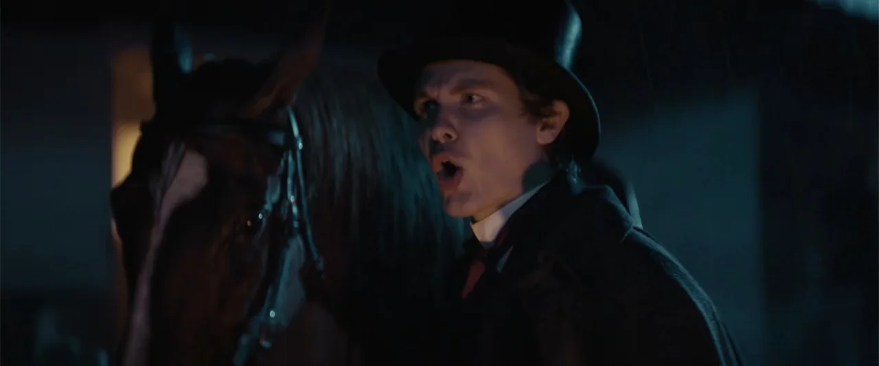 I Heard the Bells (2022) movie still: medium — A dark outdoor space at night with a horse present. A young man wearing a top hat shouts while…