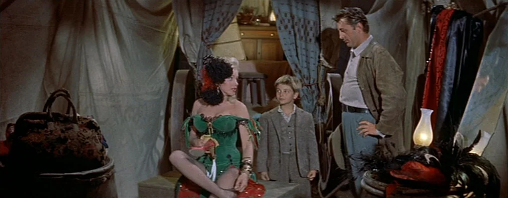 River of No Return (1954) movie still: medium — A cluttered canvas tent interior features draped fabric walls and antique traveling trunks. A woman…