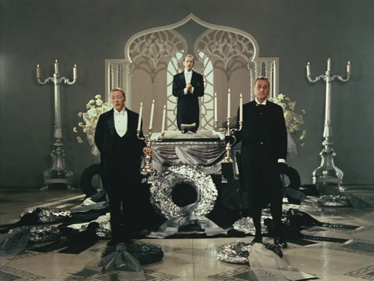 All These Women (1964) movie still: fullbody — An ornate interior funeral parlor features a central coffin draped in dark fabric. Three men in…