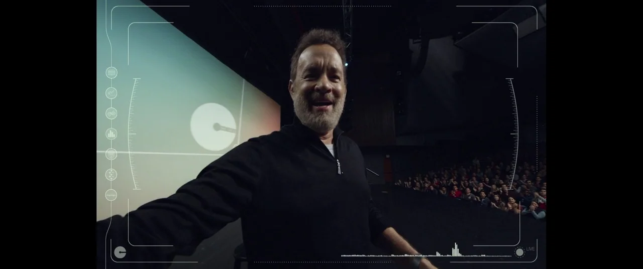 The Circle (2017) movie still: medium — A man stands on a darkened stage before a large projection screen displaying simple graphics. He holds a…