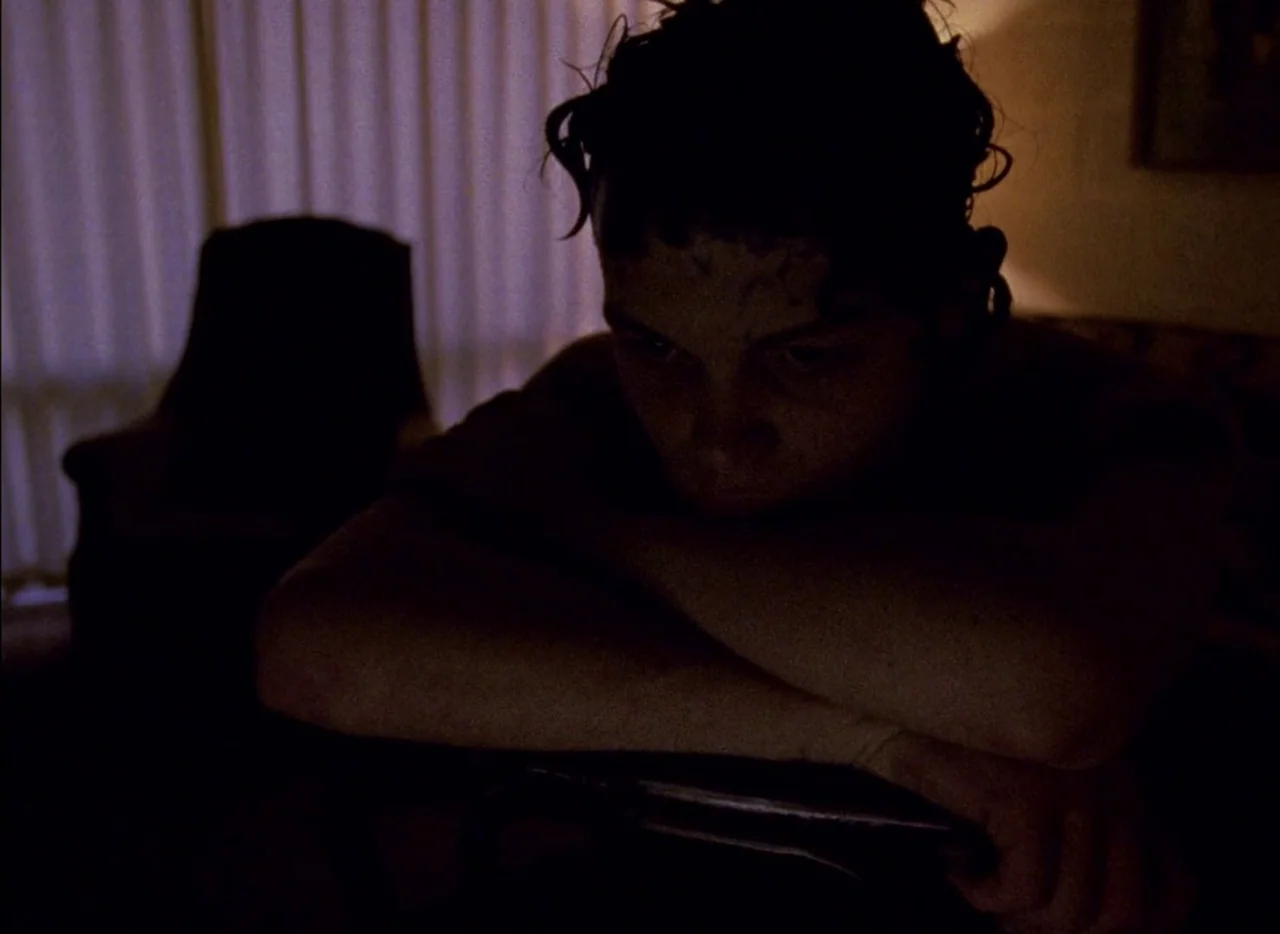 Streetwise (1984) movie still: closeup — A dimly lit room features a person sitting at a table with drawn curtains. The subject leans forward with…