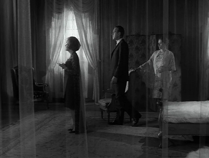 Hour of the Wolf (1968) movie still: fullbody — An opulent hotel room with sheer curtains and a vintage folding screen backdrop. A man in a suit…