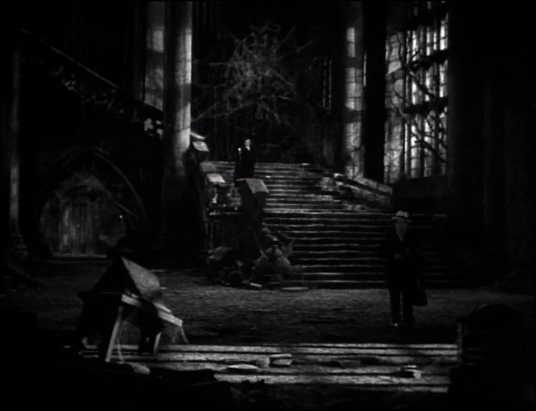 Dracula (1931) movie still: wide — A dark, dilapidated mansion foyer with a grand stone staircase and cobwebs. A man in a suit walks across the…